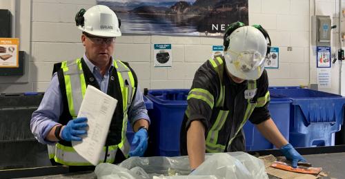 Two people in hard hats and vests sorting in a facility.