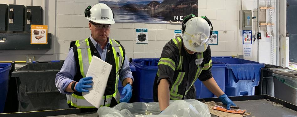 Two people in hard hats and vests sorting in a facility.