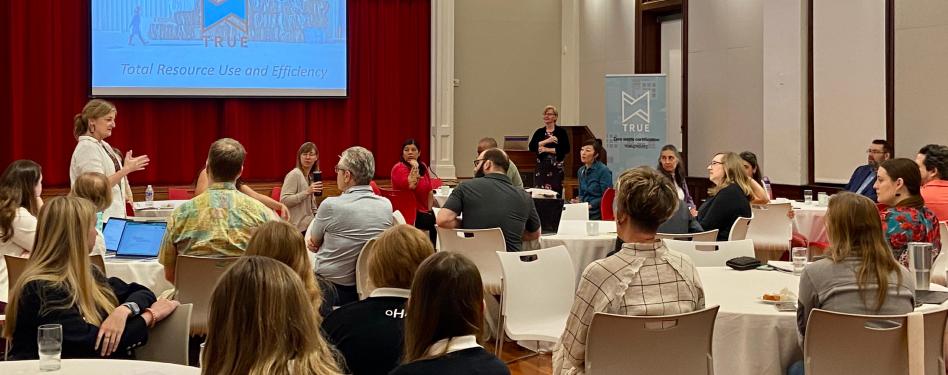 A crowd of people at tables in a TRUE presentation